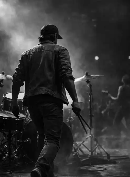 Photo of a young musician stepping onto a concert stage to play drums as the crowd cheers.